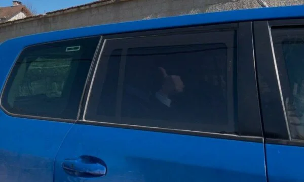 Thaci vede oltre il vetro nero dell'auto EULEX puntando le dita mentre lascia casa