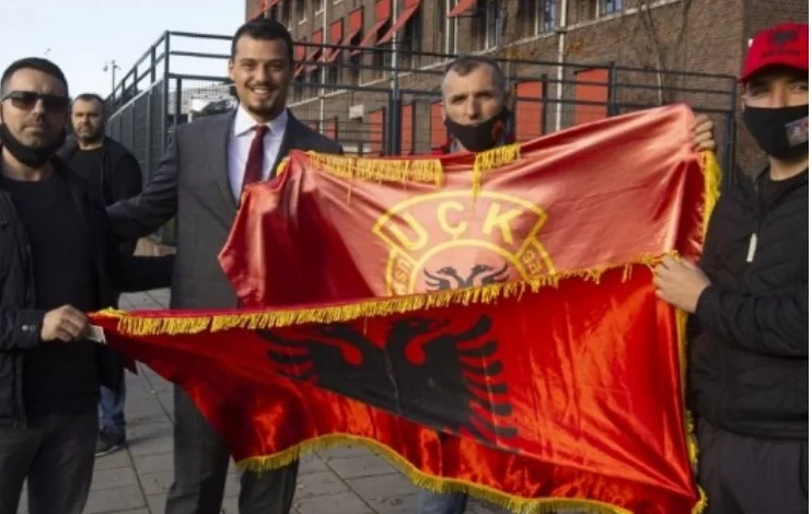 Andrew Thaci devant le siège de La Haye avec un drapeau rouge et noir sur les mains