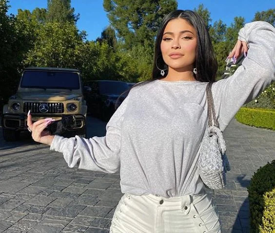 Kylie me poza në oborrin e shtëpisë, pranë makinave luksoze